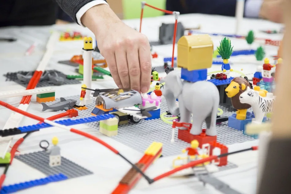 Des mains construisent et déplacent des modèles sur une table d’atelier, archive Opopoï